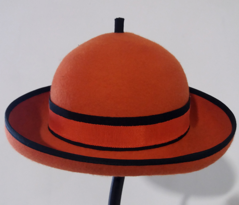 Chapeau melon en feutre rouge avec deux bandes noires sur fond gris.